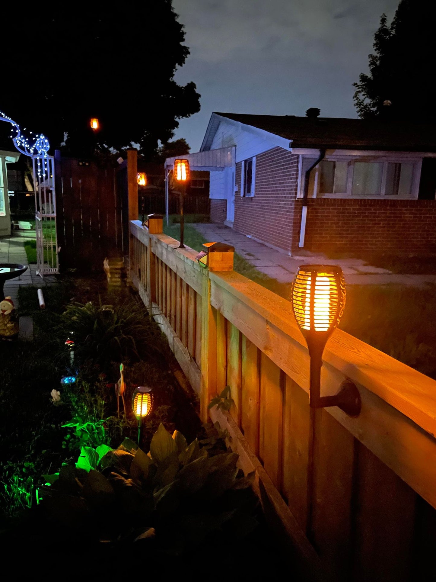 BigM 96 LED Solar Flickering Dancing Flame Lights with Wall mount is installed at the side of fence post by the garden